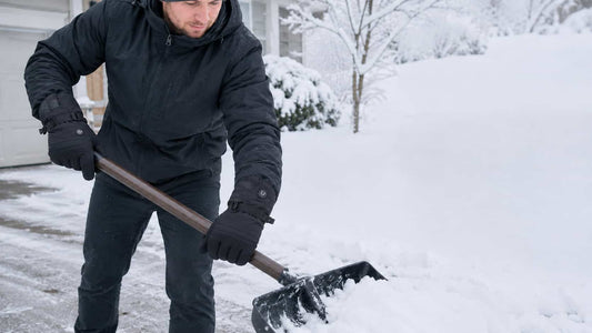 Person wearing black WinterGlow heated gloves while shoveling snow from a residential driveway