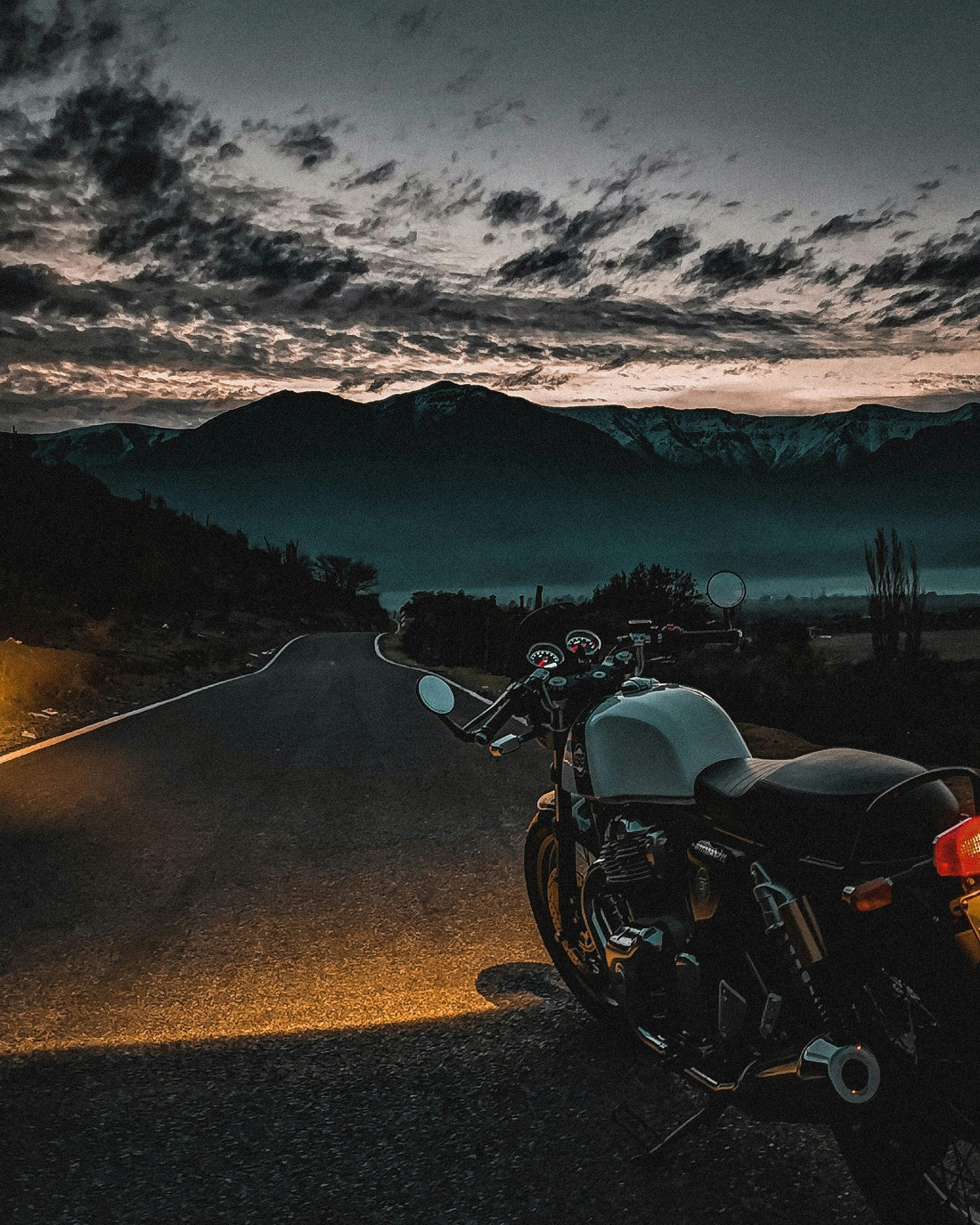 A classic touring motorcycle parked on a mountain highway road facing a cold weather inversion and snow peaks, illustrating how to keep hands warm and prevent motorcycle hand numbness.