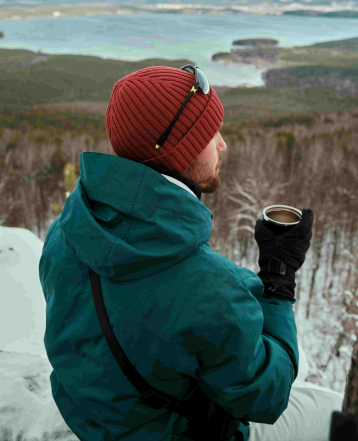 A man wearing Arcfomor heated gloves is enjoying his coffee on a winter day.