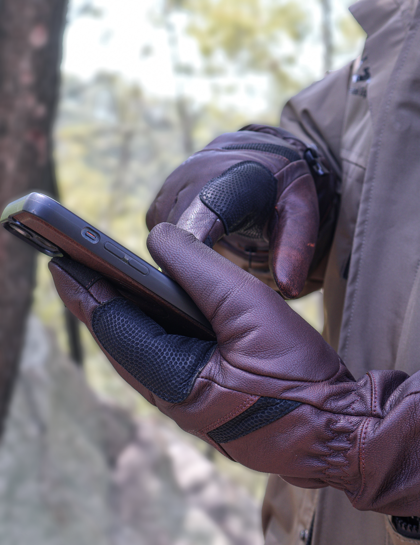 A man in the field wearing Vellum heated gloves is operating a smartphone.