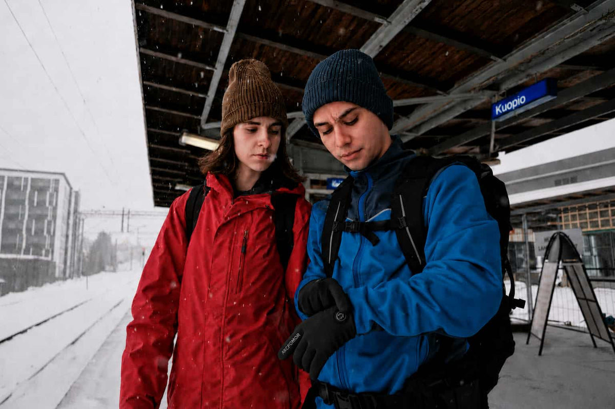 Commuters wearing Arcfomor Feather thin heated gloves at a snowy winter station