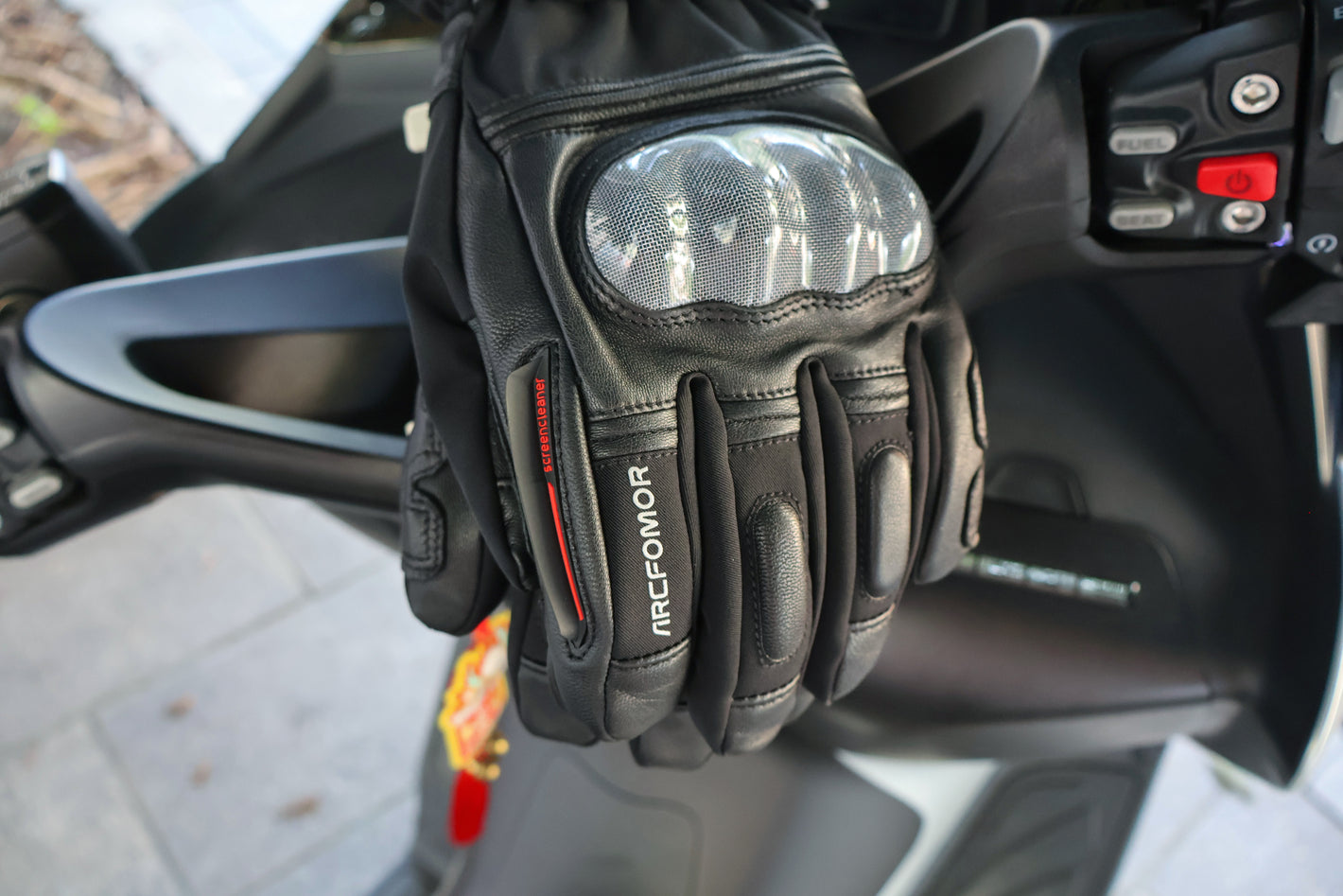 Basalt glove worn beside a motorcycle with the index-finger visor wiper clearly visible