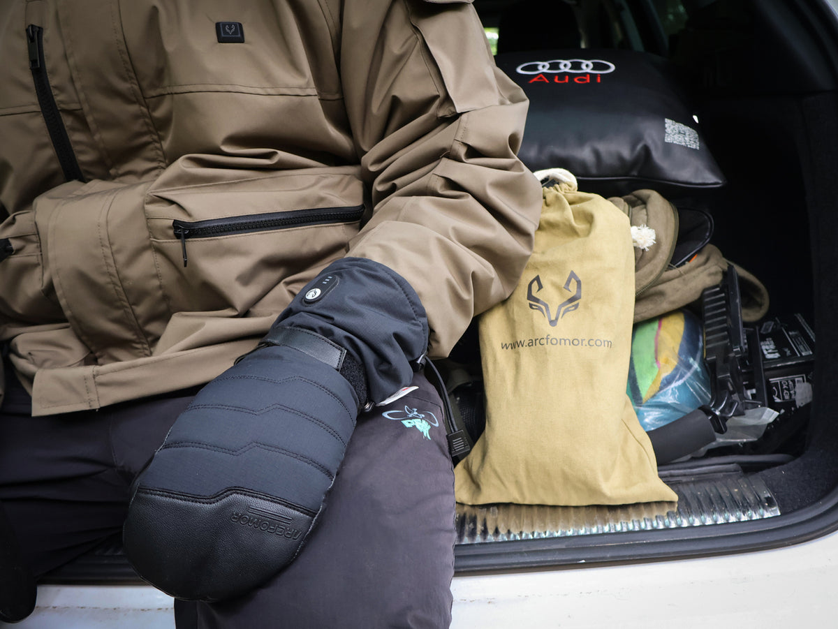 Person wearing Niagara Stone heated mittens while preparing winter hiking gear at a vehicle