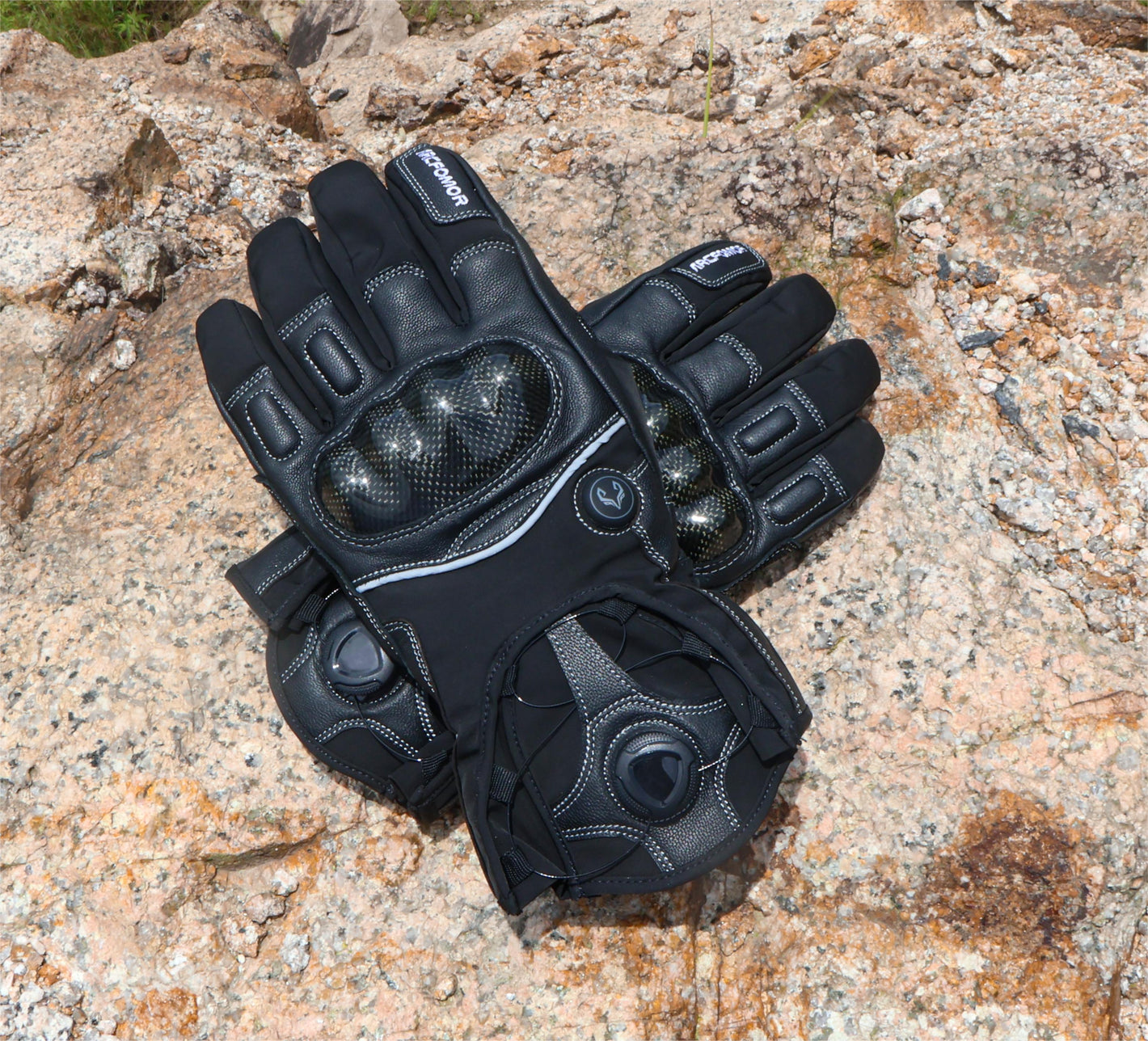 Black Onyx heated motorcycle gloves displayed outdoors, showing the carbon-fiber knuckle shells and short rotary-dial cuffs
