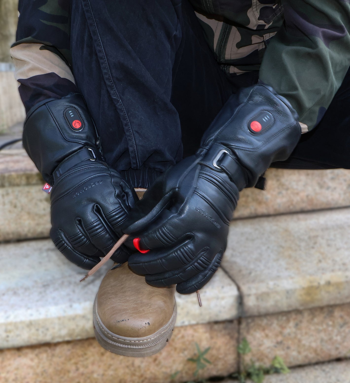 Person wearing Polar Baron heated gloves while lacing a hiking boot outdoors
