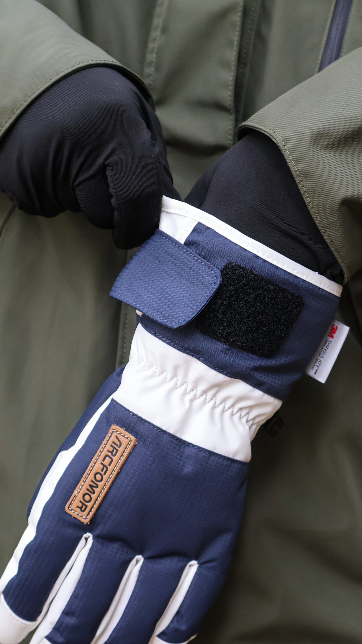 Person pulling a white and navy Summit of Kunlun shell glove over a separately sold heated liner