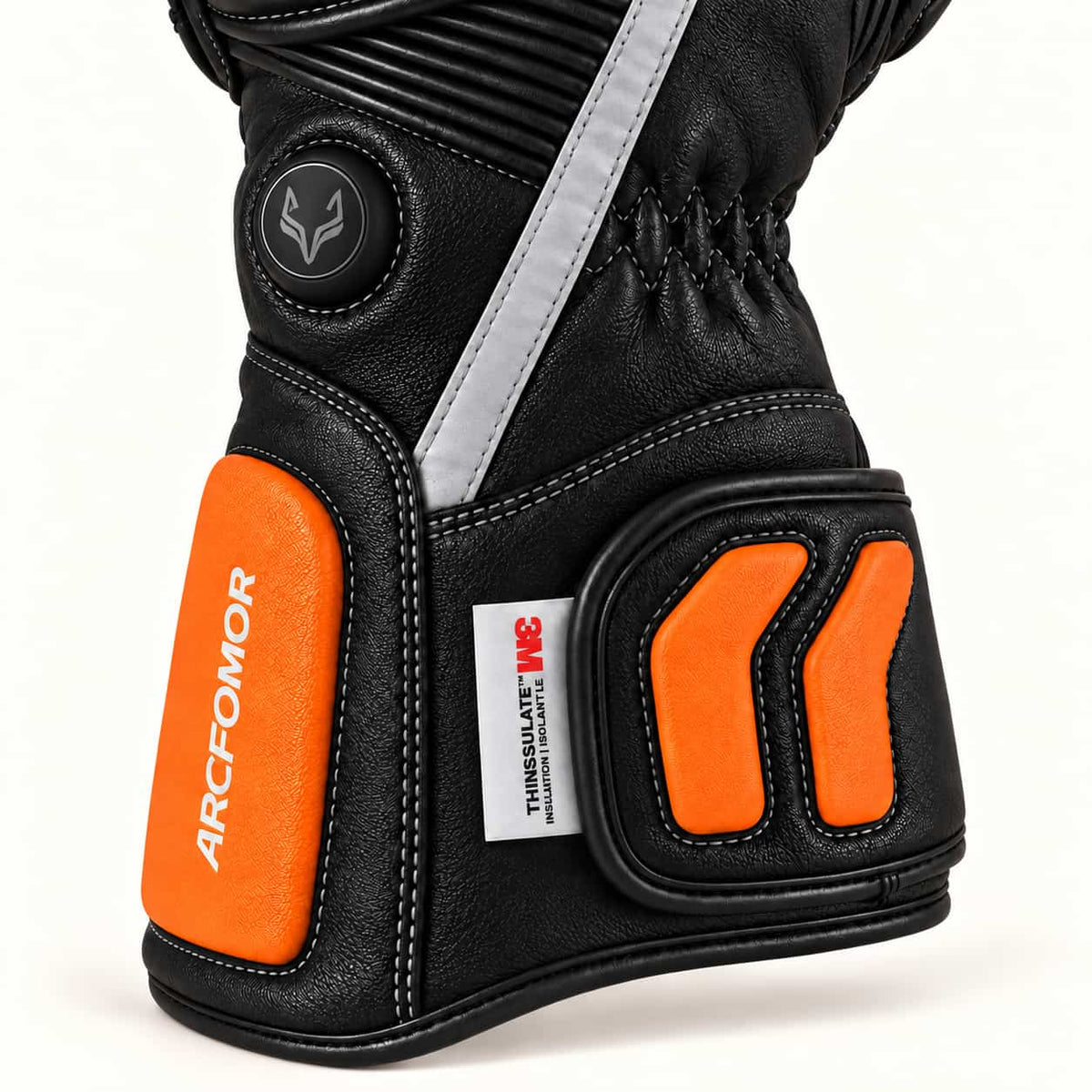 Tempest glove close-up showing the round fox-logo heat control, reflective strip and orange leather cuff details.