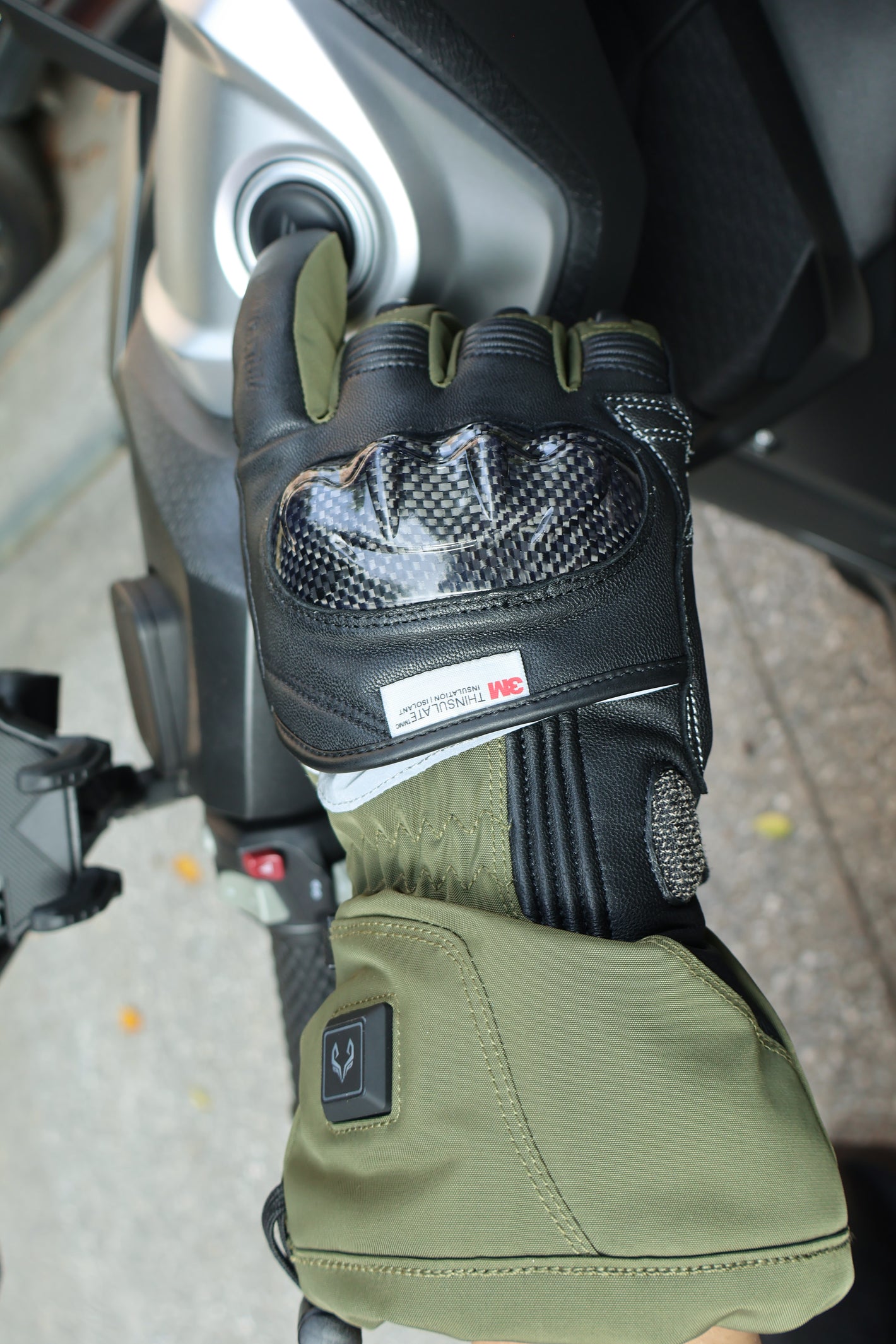 Vortex heated motorcycle glove beside a motorcycle ignition and handlebar