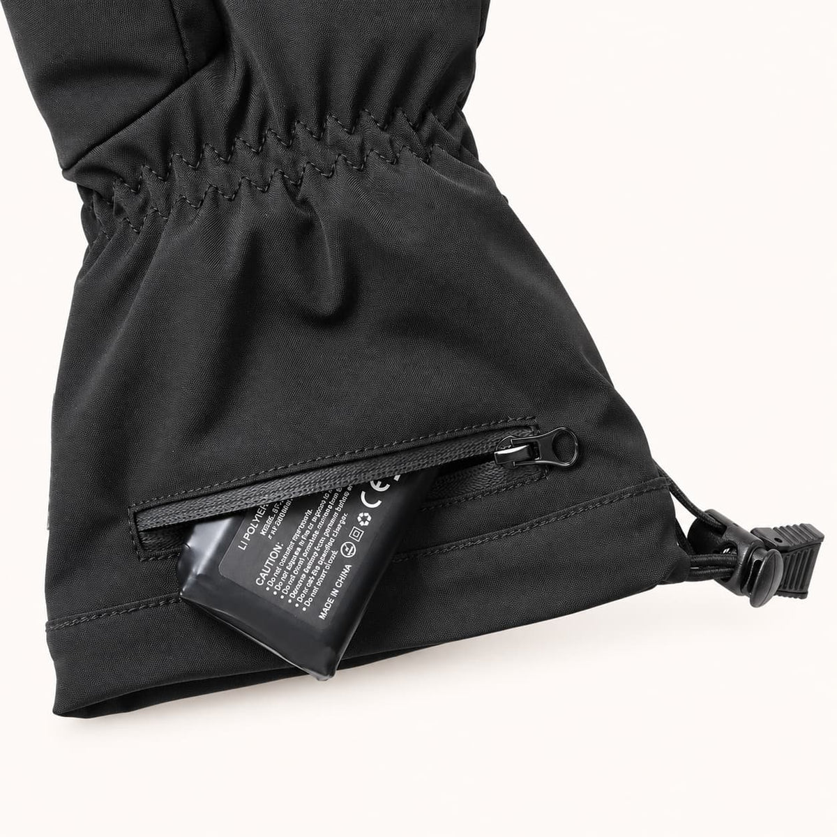 A rechargeable battery partially exposed through the WinterGlow glove’s zippered cuff pocket.