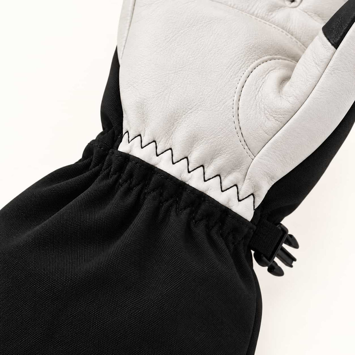 Close-up of the zigzag seam joining the white goatskin palm to the black elastic wrist on a Yellowstone glove.